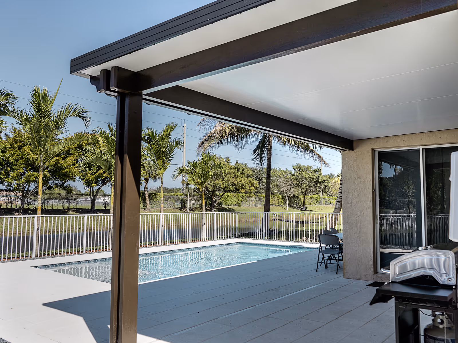 Cubierta de patio de aluminio junto a una piscina con palmeras en el sur de Florida
